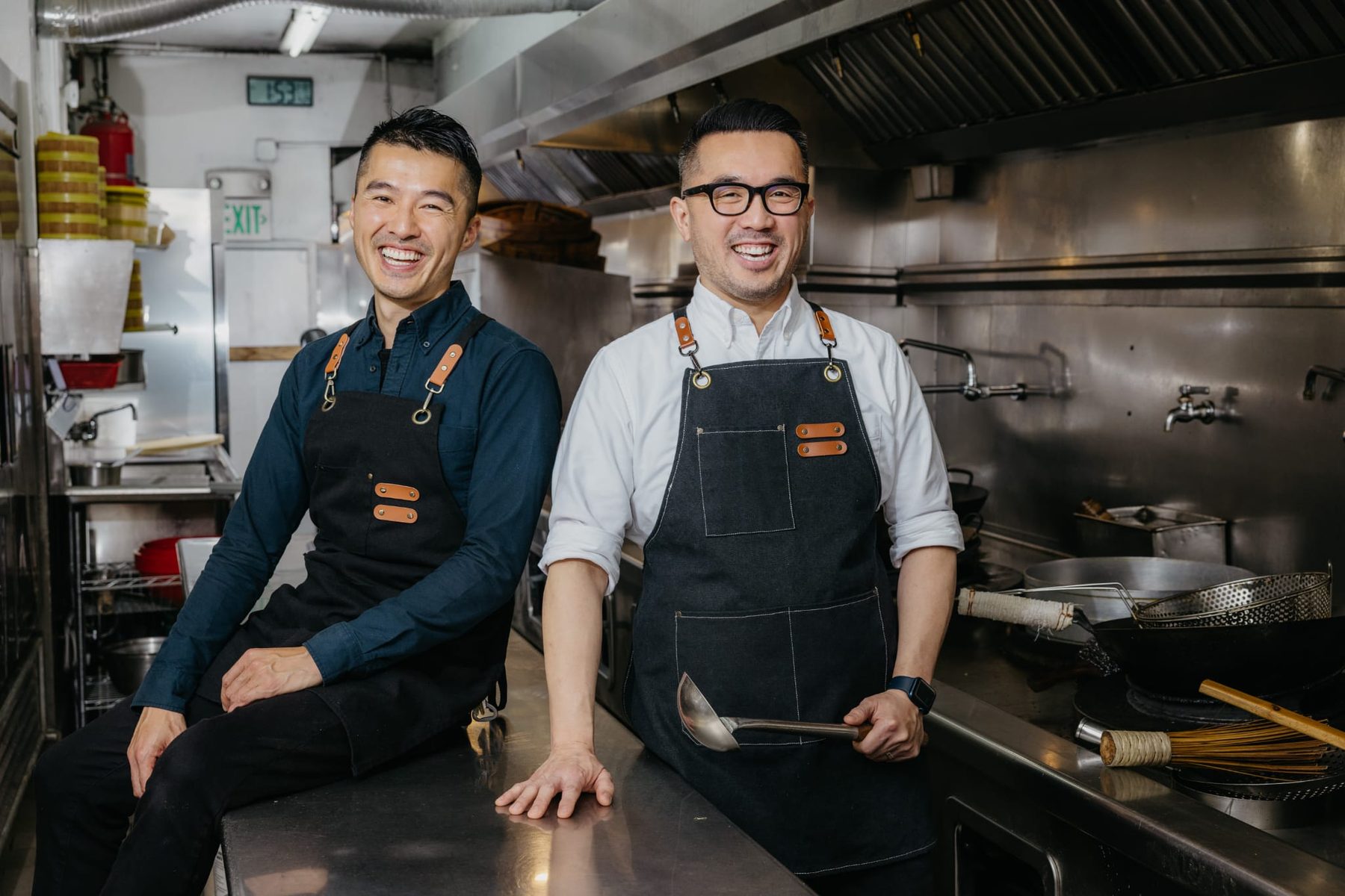 Two chefs smiling together in a Chinatown restaurant kitchen